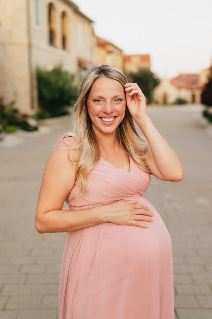 A woman in pink dress holding her pregnant belly.