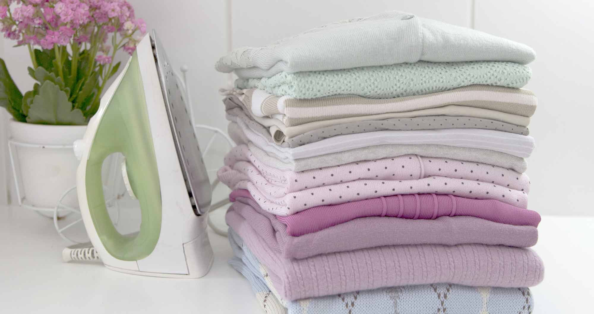 A stack of folded clothes next to an ironing board.